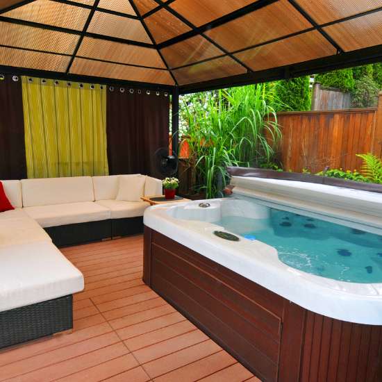 Backyard remodeling in San Diego with a jacuzzi and comfortable seating area under protective netting, flanked by lush plants and privacy drapes.